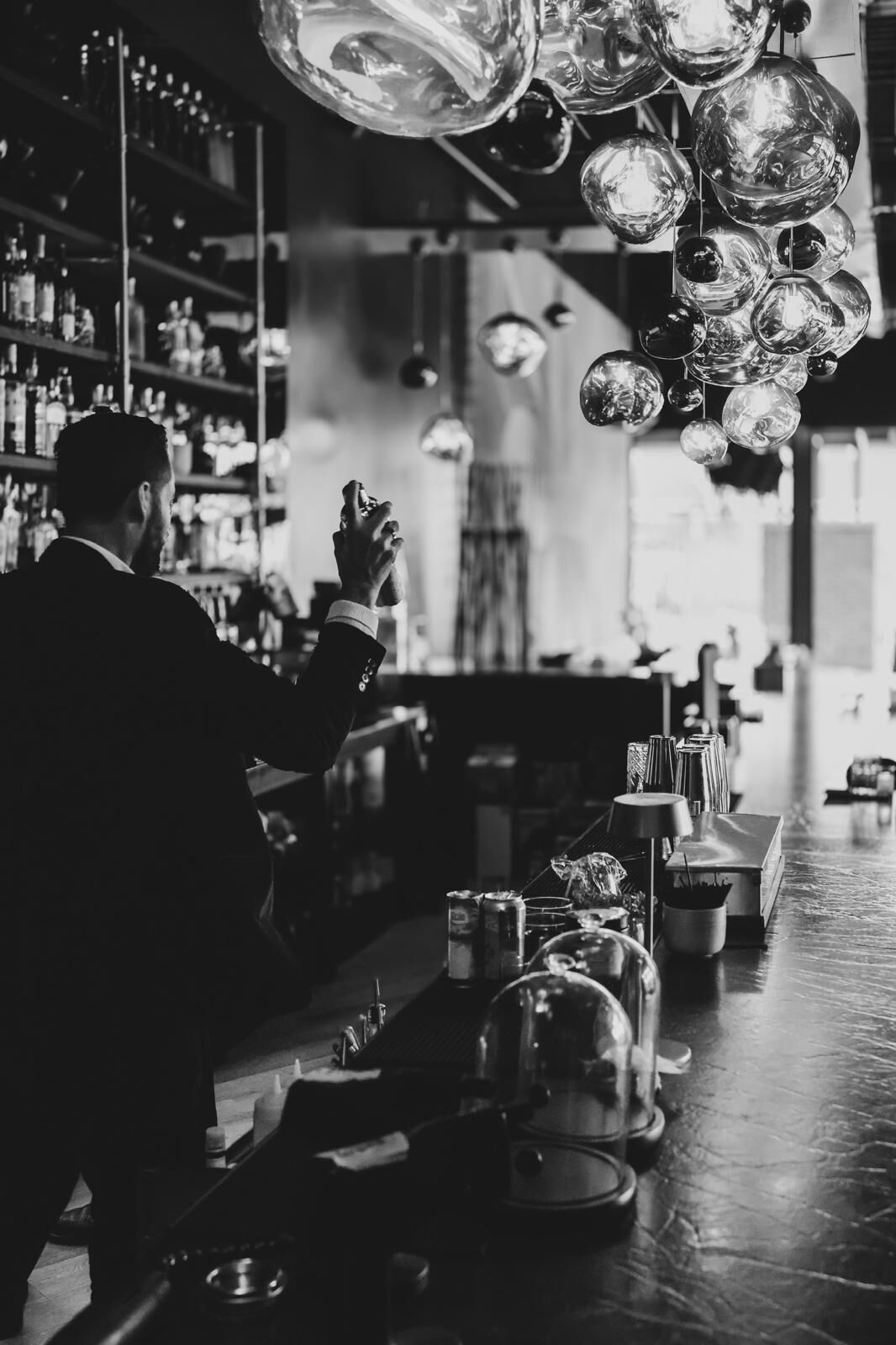 A bartender in a suit shaking a cocktail beneath Olé's glass pendants
